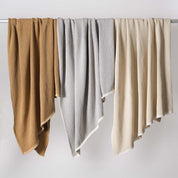 Three in2green Checkerboard Throw Blankets in brown, gray, and cream hang over a horizontal rod against a plain white background.