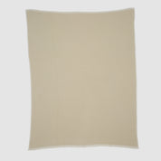 The Checkerboard Throw Blanket is a beige, rectangular knit with a subtle textured pattern and white trim, crafted from sustainable upcycled cotton—perfect for adding cozy style to any space. Shown flat on a plain white background.
