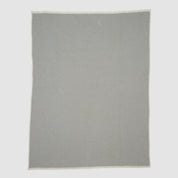 The Checkerboard Throw Blanket is a rectangular, light grey mini throw made from sustainable upcycled cotton with a subtle geometric pattern and off-white edges—perfect for cozy living and displayed on a plain background.