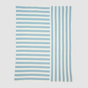 The Coastal Stripes Throw Blanket features horizontal light blue and white stripes on the left and vertical stripes on the right, creating a breezy seaside-inspired look against a plain background.
