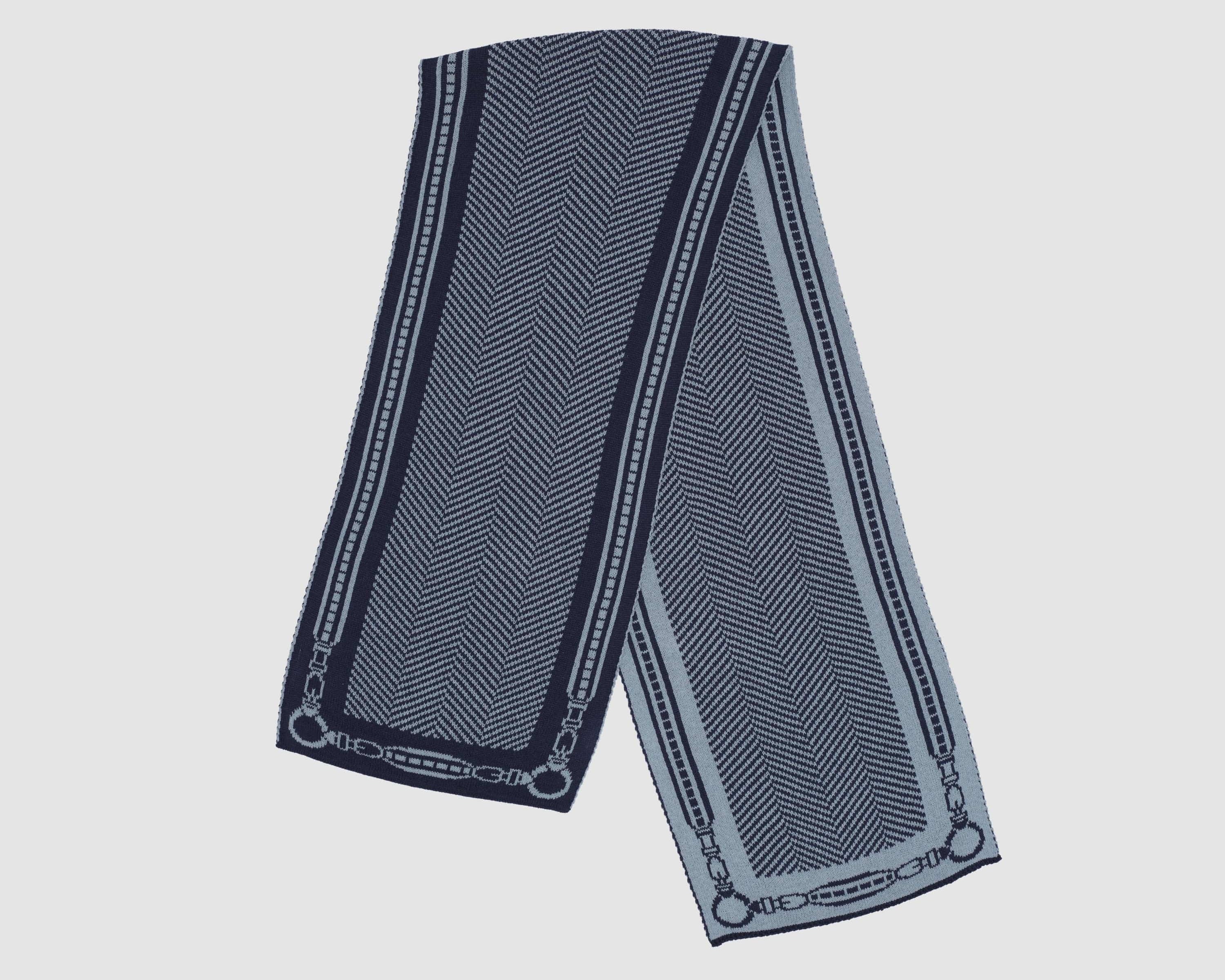 The Equestrian Harness Herringbone Scarf is a rectangular navy blue scarf featuring a herringbone pattern and chain-inspired border, made from recycled materials and shown against a plain light backdrop.