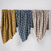 Three patterned blankets—including the in2green Gingham Plaid Throw Blanket—hang side by side over a horizontal rod, displayed against a plain white background.