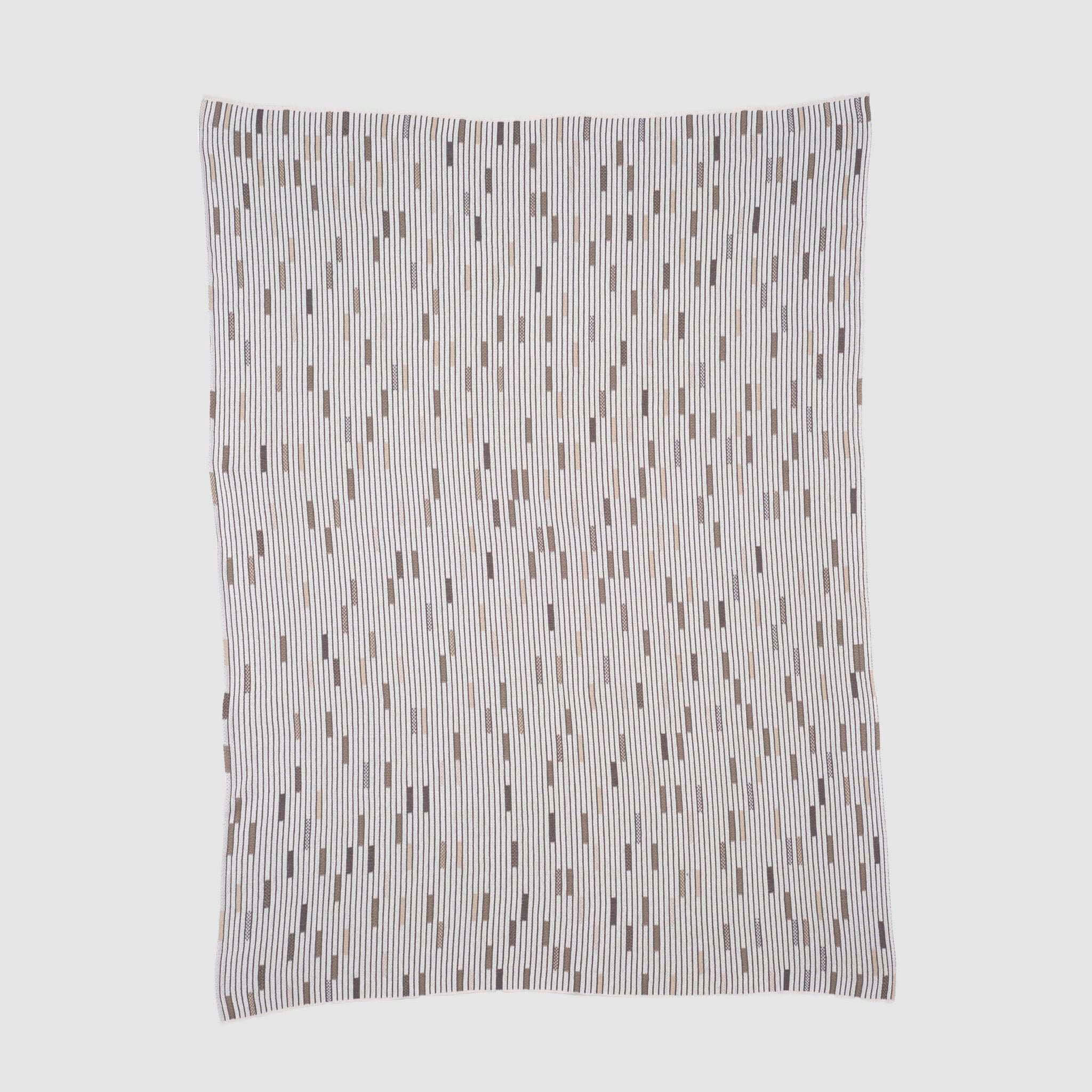 The Matrix Throw Blanket by Elodie Blanchard for in2green features thin, uneven vertical stripes and small rectangles in neutral tones on white, crafted with sustainable design principles.