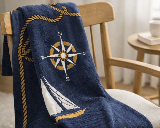 Navy blue blanket with compass and sailboat design draped over a chair.