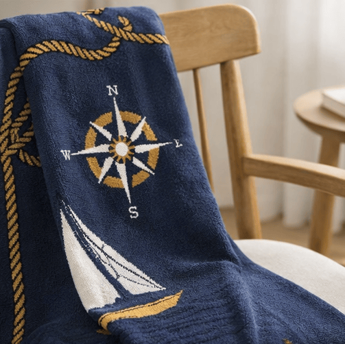 Navy blue blanket with compass and sailboat design draped over a chair.
