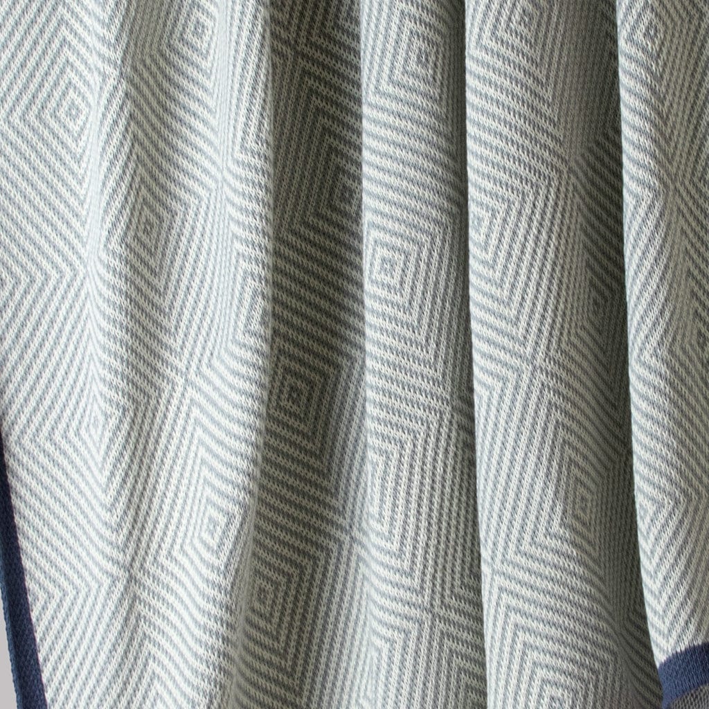 Close-up of the in2green Poly Woven Square Throw Blanket, featuring light gray outdoor fabric with a geometric diamond pattern and textured folds; sustainably crafted from recycled plastic bottles.