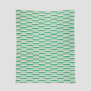 The Riata Throw Blanket by Petra Kaksonen for In2Green features a Scandinavian-inspired design with horizontal green and beige rectangles on a light background—perfect for stylish, sustainable home decor.