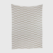 The Riata Throw Blanket by Petra Kaksonen is a rectangular white blanket with staggered rows of beige rectangles, inspired by Scandinavian heritage.