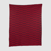The Riata Throw Blanket by Petra Kaksonen is a rectangular red piece inspired by Scandinavian heritage, showcasing horizontal stripes in alternating dark and bright red on a plain background.