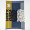 The “Rock Rose” throw by Susy Pilgrim Waters for In2Green features a modern design with a large white flower, black and white polka dots, and sections of olive green, navy blue, and patterned backgrounds.