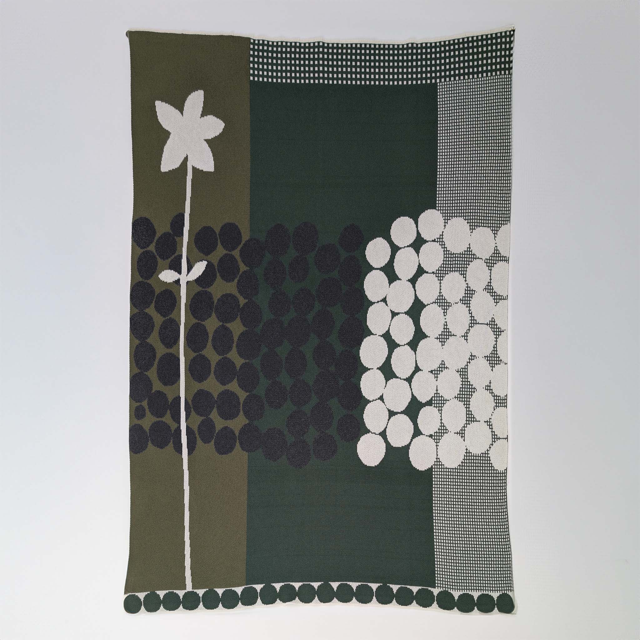 Rock Rose by Susy Pilgrim Waters for In2Green is a modern rectangular textile with a white abstract flower and black-and-white geometric circles on green, black, and white backgrounds, crafted from a sustainable cotton blend.