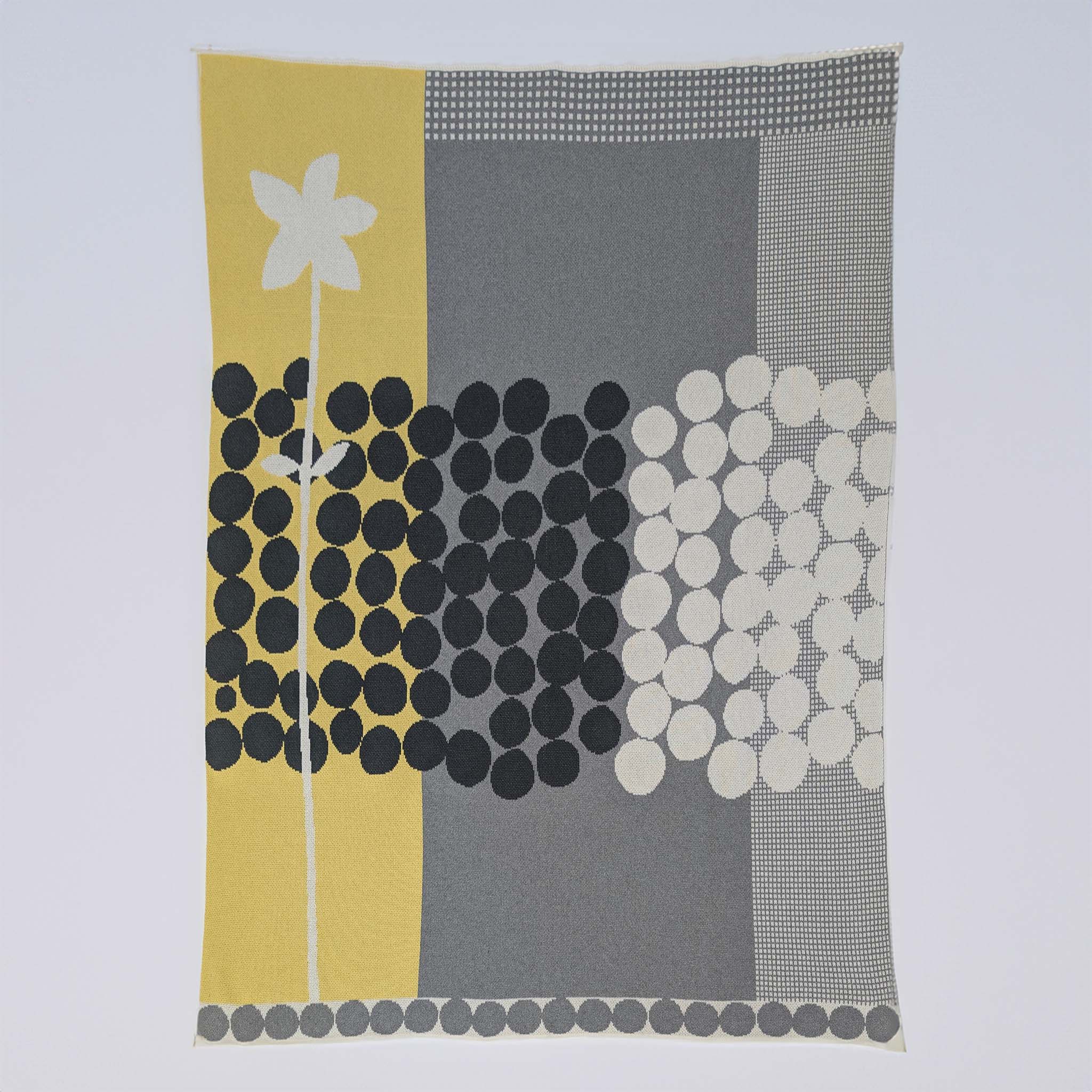 Rock Rose by Susy Pilgrim Waters for In2Green is a modern rectangular textile in yellow, gray, black, and white with abstract dots, grid designs, a vertical white flower, and made from a sustainable cotton blend.