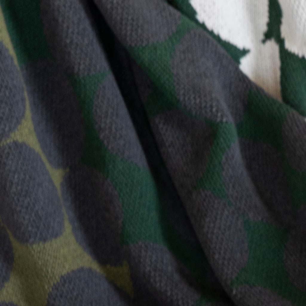 Close-up of the Cotton Sustainable Knit Floral Graphic Throw Blanket - Rock Rose by Susy Pilgrim Waters for In2Green, featuring dark gray circles on green and white accents, crafted from a sustainable cotton blend.