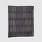 The Washed Throw Blanket by Jill Malek for In2Green features a black background with vertical beige and gray stripes in an irregular, nature-inspired pattern, reflecting Malek's organic design style.