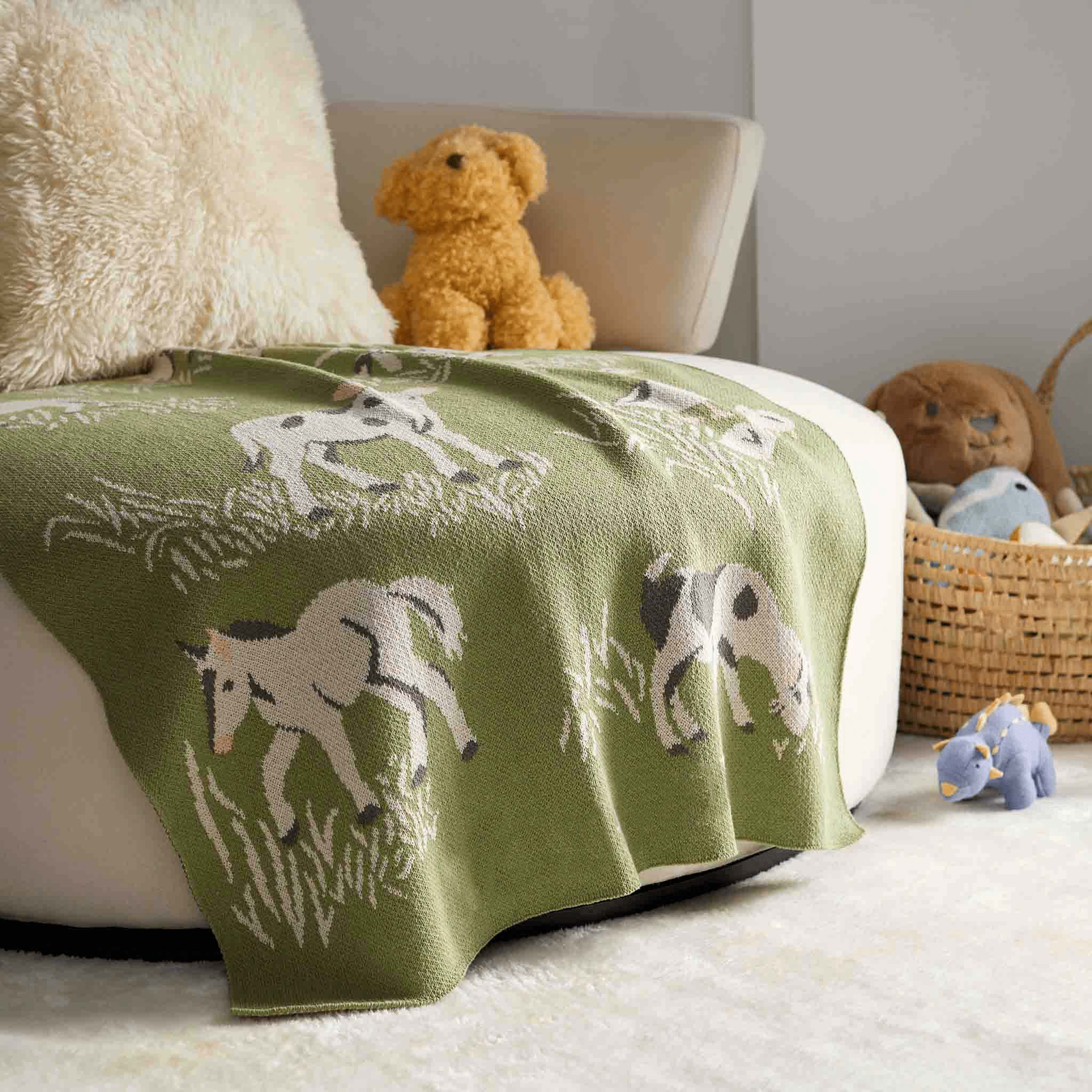 The In2Green Baby Farm Blanket is draped over a white chair in the nursery, featuring playful farm designs with stuffed animals and a wicker basket in the background.