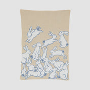 The in2green Baby Rabbits Blanket is a charming beige throw made from recycled cotton, featuring white rabbits outlined in blue, some playfully holding or playing with balls—perfect for gender-neutral decor.