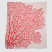 The in2green Fan Coral Throw Blanket features a light pink fabric with a bold red coral branch design—ideal for adding coastal style to beach houses or as a chic accent piece.