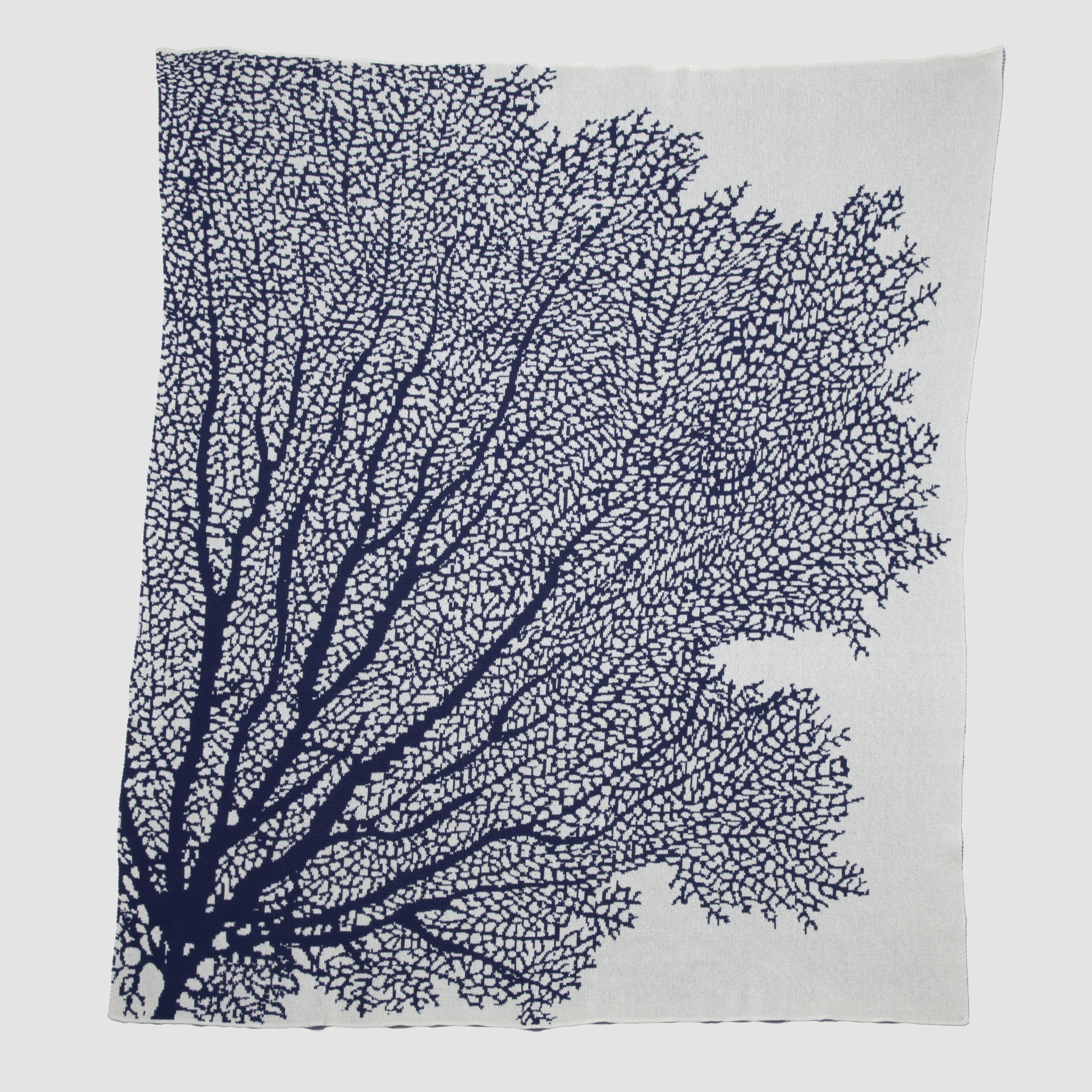 The Fan Coral Throw Blanket by in2green features white fabric adorned with a dark blue, coral-like pattern branching from the bottom left, perfect for enhancing coastal style in beach houses.