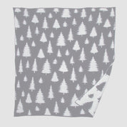 A nature-inspired gray throw with a white pine tree pattern, slightly turned at the corner to show its reverse color scheme, adds a unique twist to in2green's Fir Trees Reversible Throw Blanket.