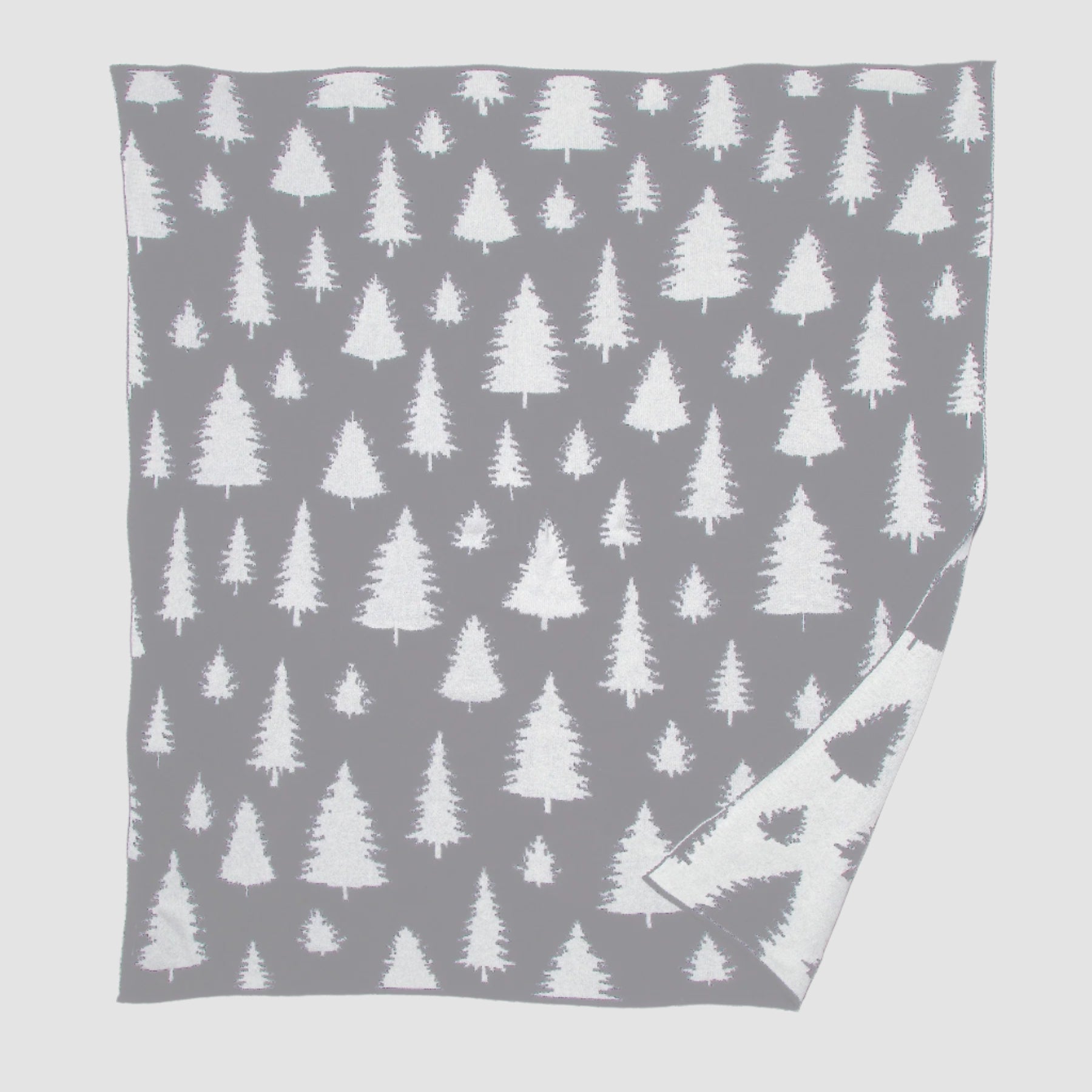 A nature-inspired gray throw with a white pine tree pattern, slightly turned at the corner to show its reverse color scheme, adds a unique twist to in2green's Fir Trees Reversible Throw Blanket.
