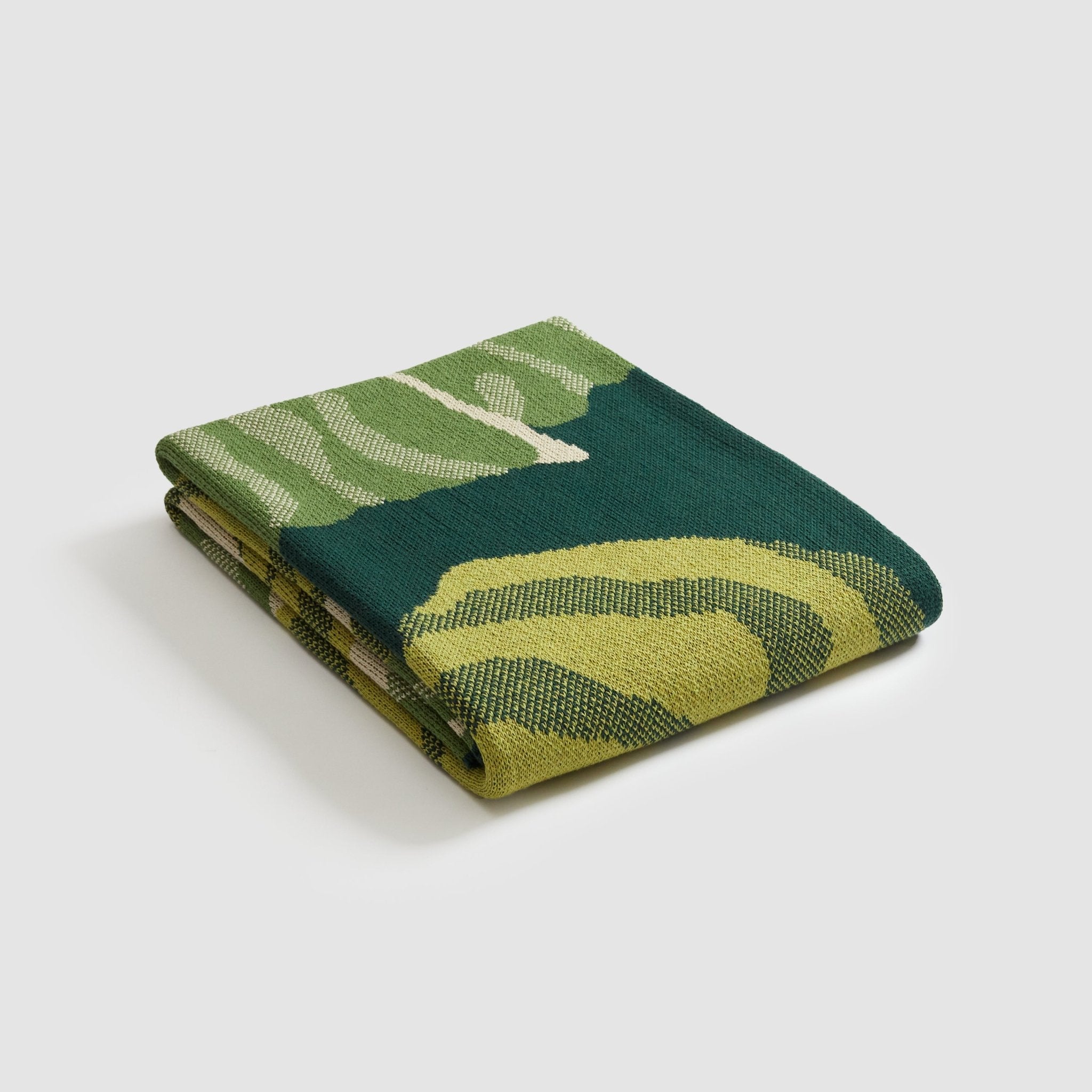 A Floréal 7 Throw Blanket by in2green rests elegantly on a white surface, featuring green and yellow patterns. Crafted from recycled cotton, it embodies an Art Nouveau style.