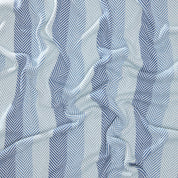 Close-up of crumpled Herringbone Hues Throw Blanket by In2Green, showcasing a zigzag pattern with alternating dark and light blue stripes, made from recycled cotton.