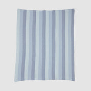 The Herringbone Hues Throw Blanket by In2Green is crafted in the USA from recycled cotton. Featuring alternating light and dark blue herringbone stripes on a white background, it combines style and sustainability for any setting.