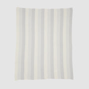 The Herringbone Hues Throw Blanket from In2Green, made in the USA with recycled cotton, features a rectangular design with alternating vertical stripes in light gray and off-white against a plain background.