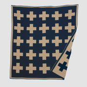 The Swiss Cross Reversible Throw Blanket by in2green has a reversible design with beige plus signs on dark blue, enhancing any ski chalet elegantly. Its neatly folded corners ensure a cozy look.