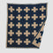 The Swiss Cross Reversible Throw Blanket by in2green has a reversible design with beige plus signs on dark blue, enhancing any ski chalet elegantly. Its neatly folded corners ensure a cozy look.