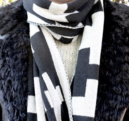 Close-up of a person adorned in an in2green Eco Swiss Cross Reversible Scarf, paired with a white sweater and a black fur-textured coat, highlighting the distinctive black and white pattern.